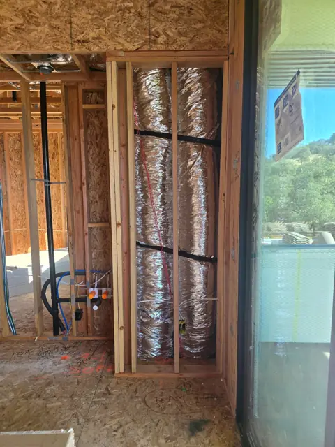 Two insulated HVAC ducts run vertically through a framed wall cavity before drywall at the Greyson Creek Drive project in El Dorado Hills